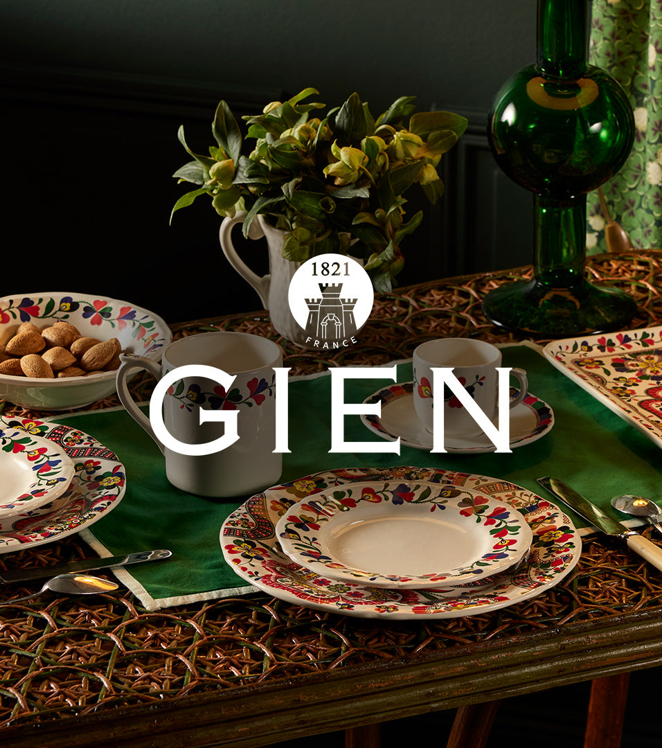 Decorative table setting with Gien, including plates, cups, and a vase on a dark background.