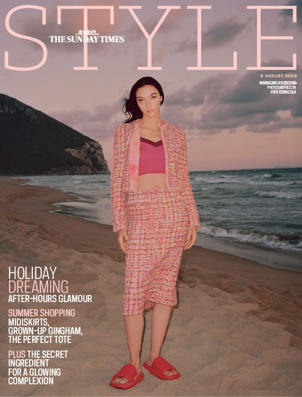 Woman in a pink outfit standing on a beach with ocean and mountain in the background, featuring 'The Sunday Times Style' magazine cover.