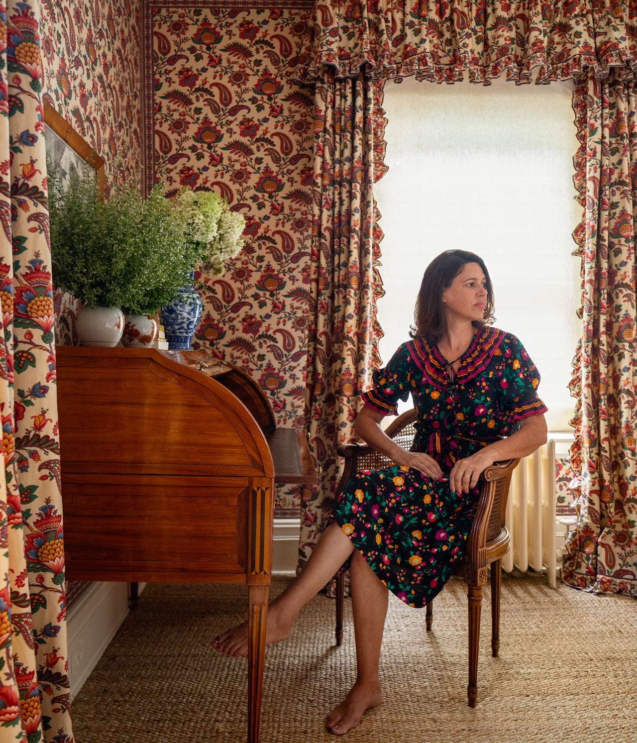 Décors Barbares founder, Nathalie-Farman-Farma sitting in front of a writing with Zénaide curtains and wallpaper.