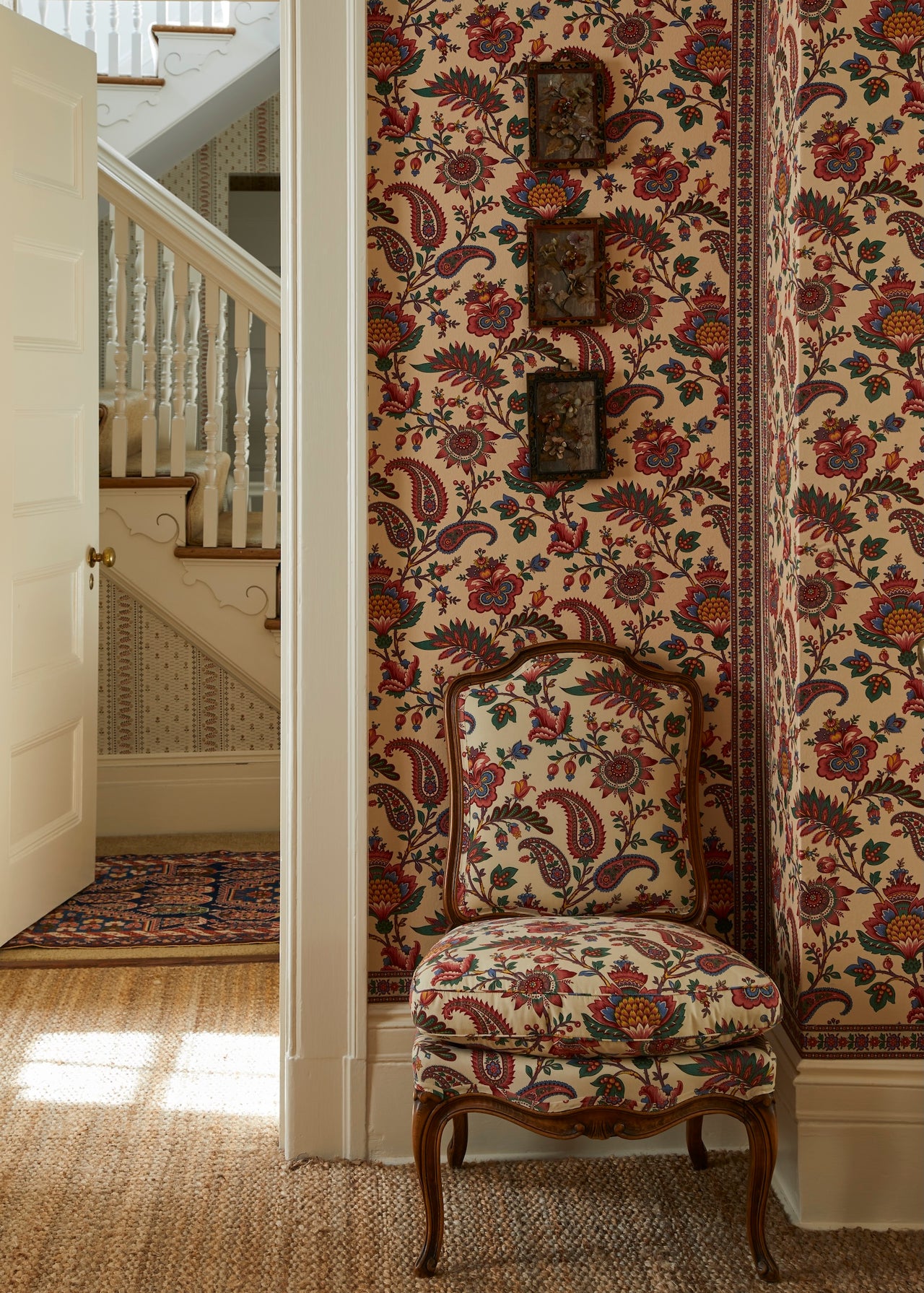 Decorative chair with floral Décors Barbares fabric against a wall with similar design, staircase in the background